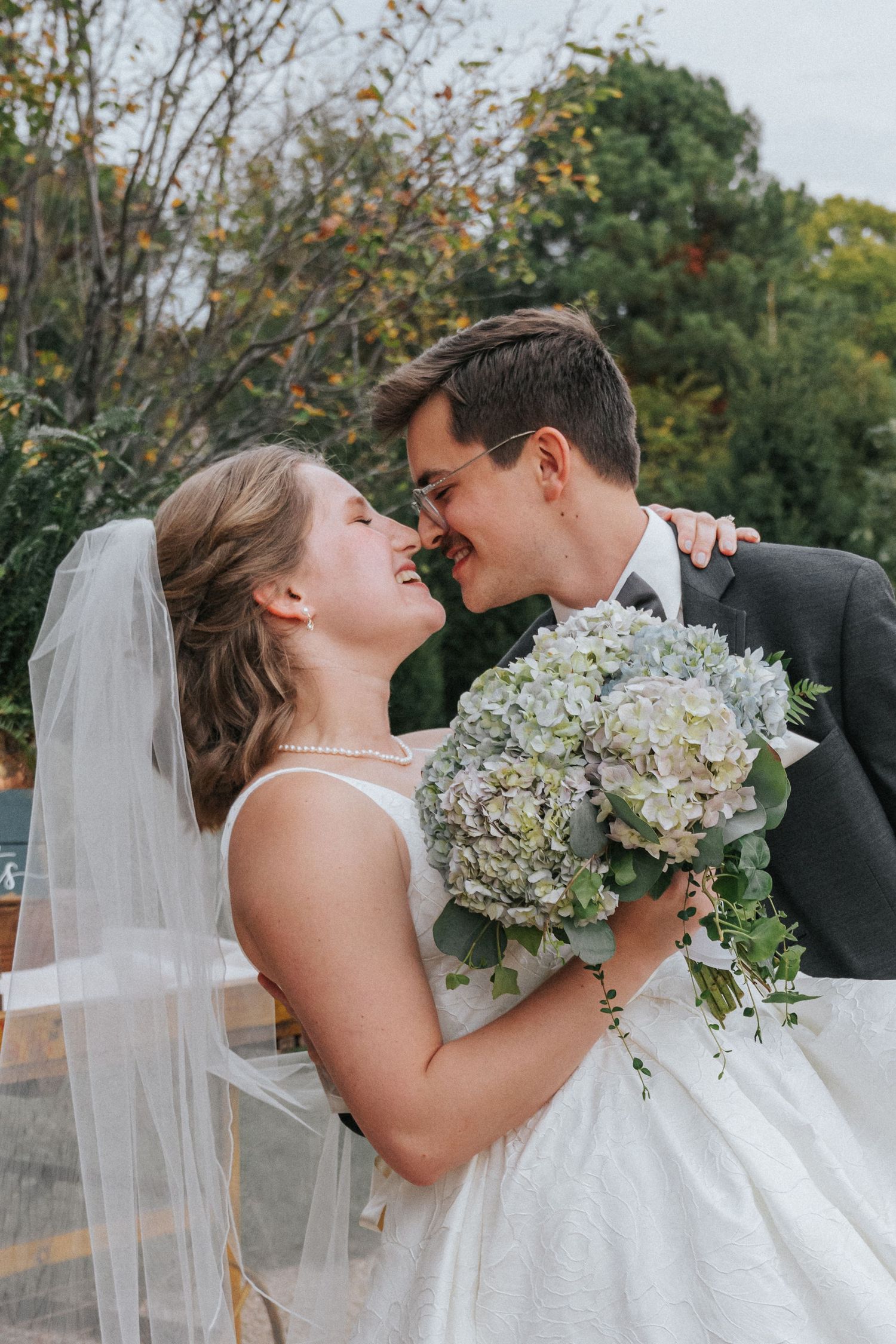 A romantic wedding couple shares intimate moments while holding a white and green hydrangea bouquet in an outdoor setting.