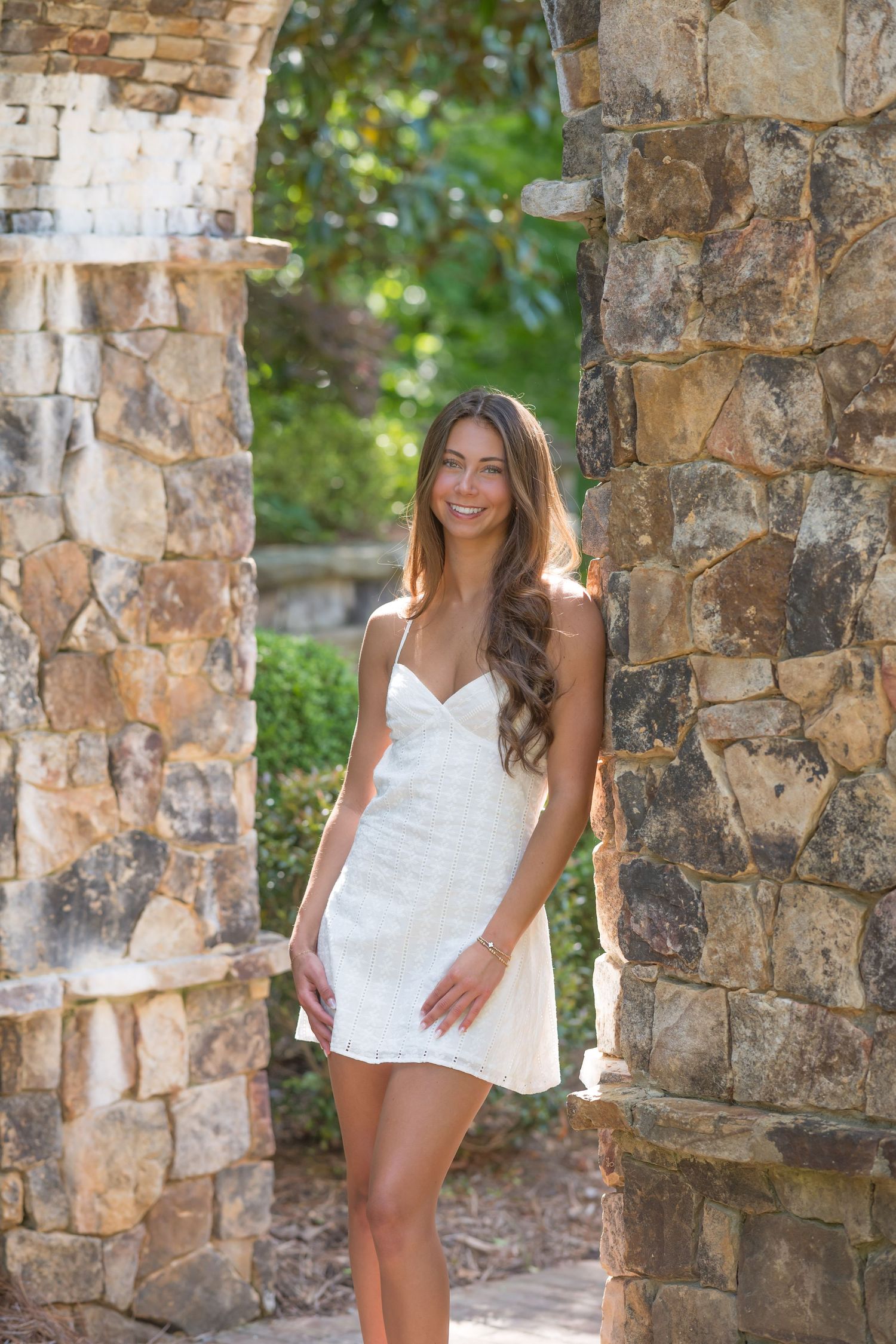 Portrait session on wooden boardwalk with pink dress against natural garden backdrop.
