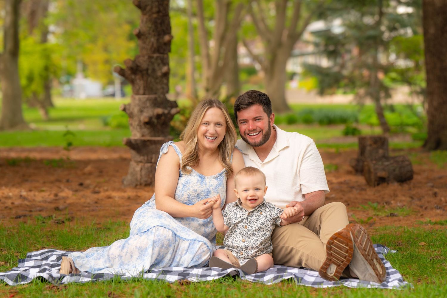 Family Photography Quad Cities. A young family sits together on a blanket in a scenic park setting surrounded by trees and autumn leaves.