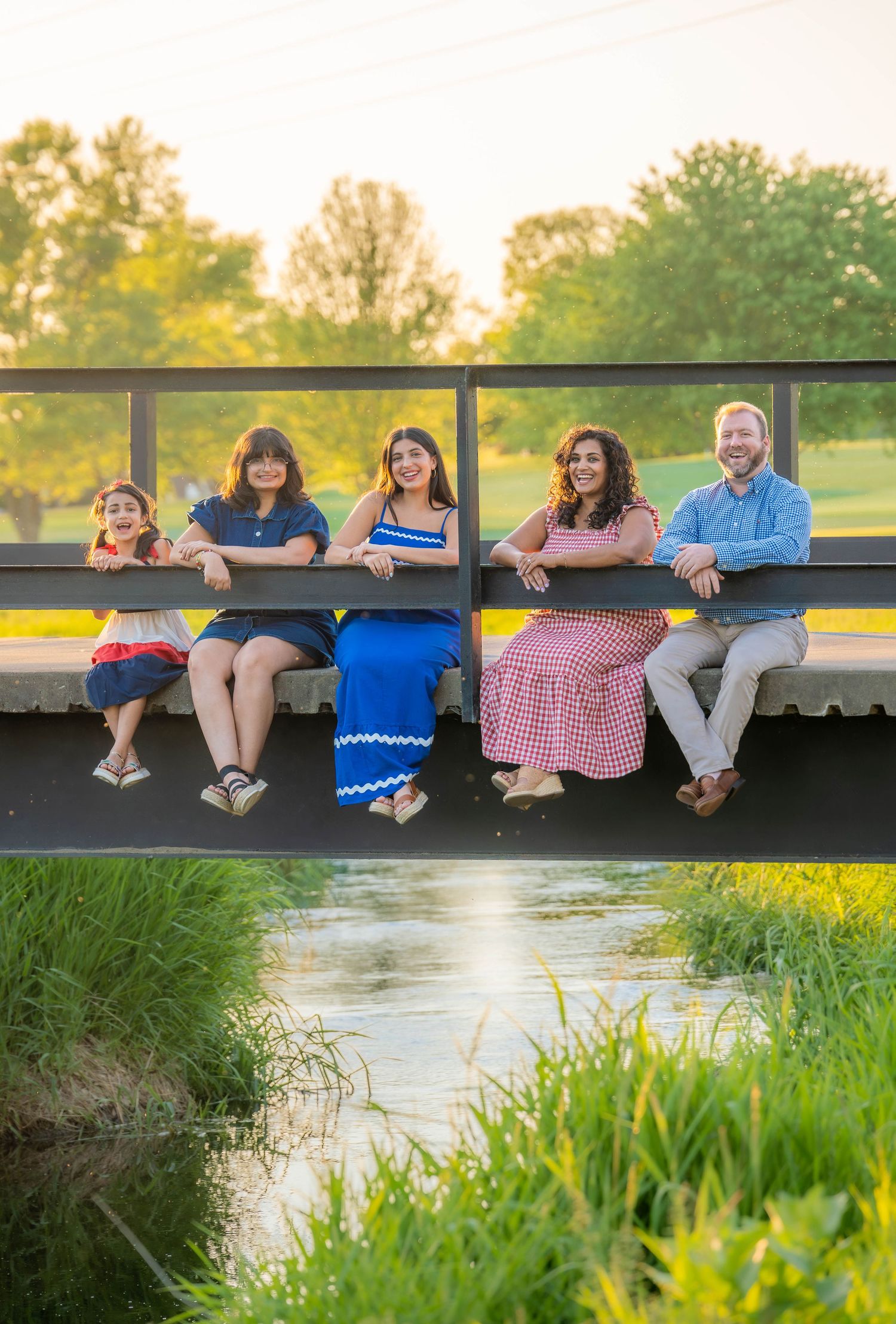 A family sits together on a wooden dock pond at sunset surrounded by lush greenery. Quad Cities Family Photography. Crow Valley Golf Club