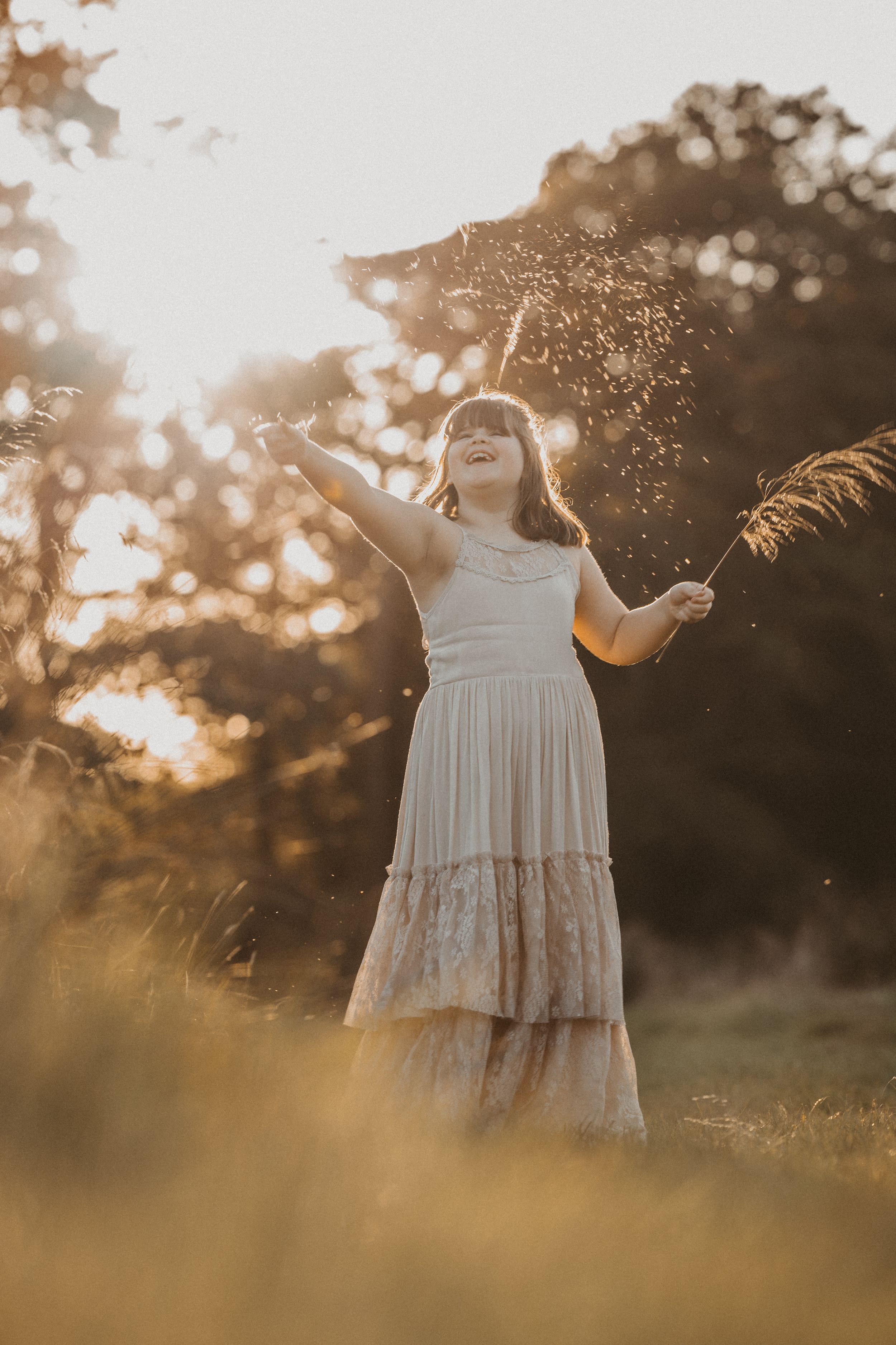 A white lace dress twirls in golden sunlight during sunset in a grassy field creating a dreamy outdoor scene.