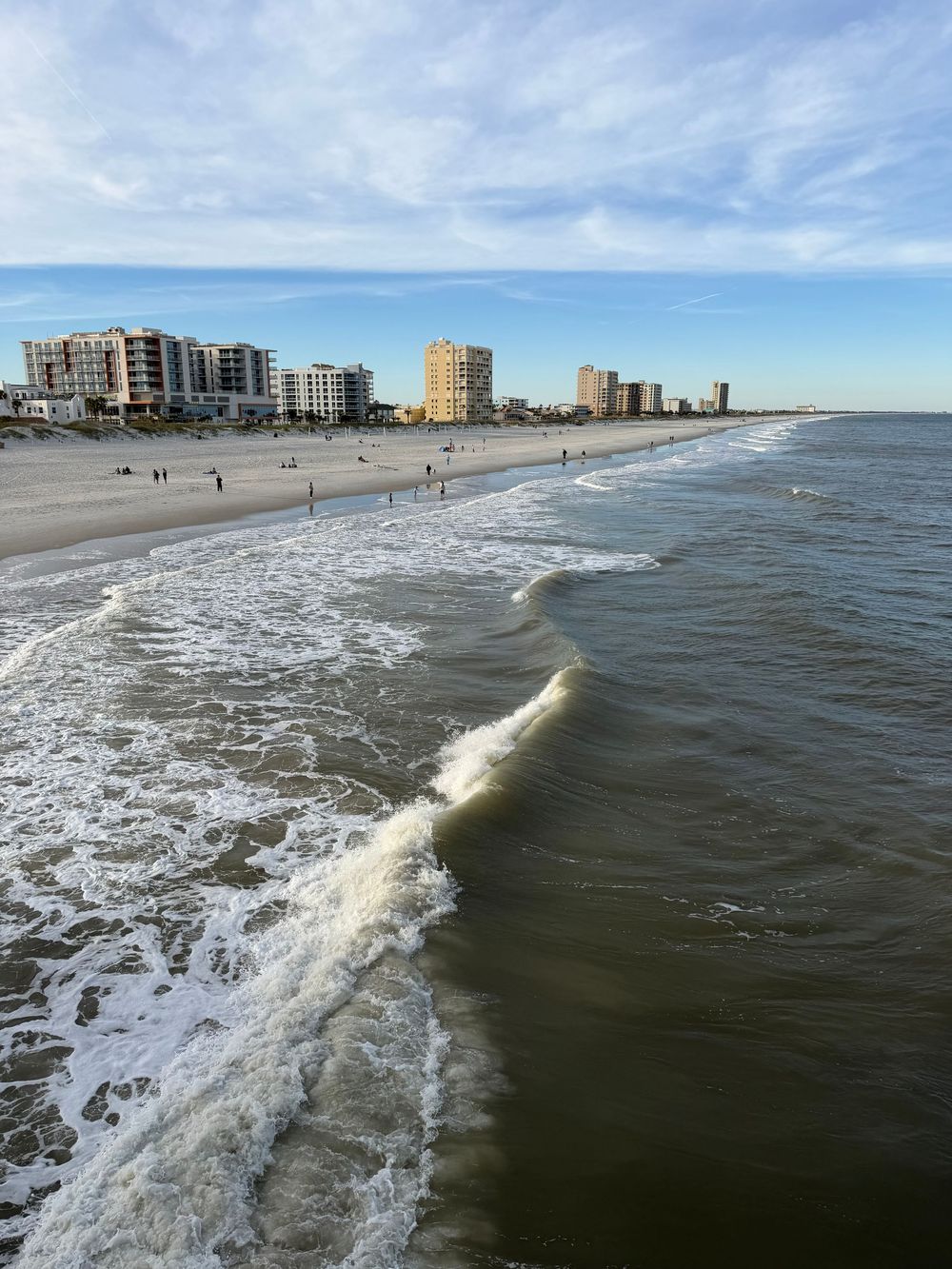 Aerial view of waves crashing along a beach with high-rise buildings lining the coast.
