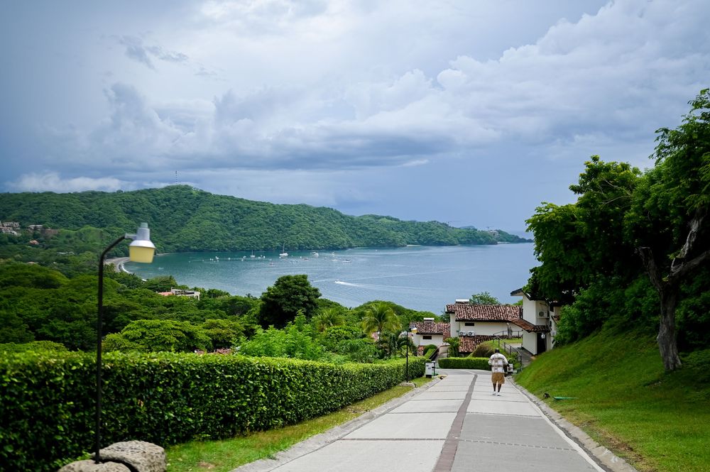 Winding road through tropical hillside with ocean views and resort buildings.
