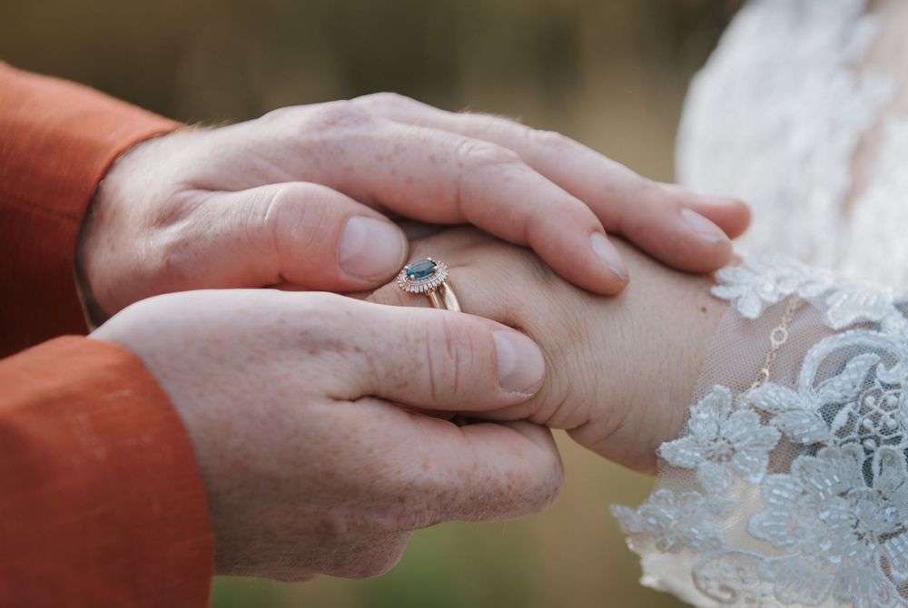 Close-up of hands exchanging wedding rings with delicate lace detail in frame.