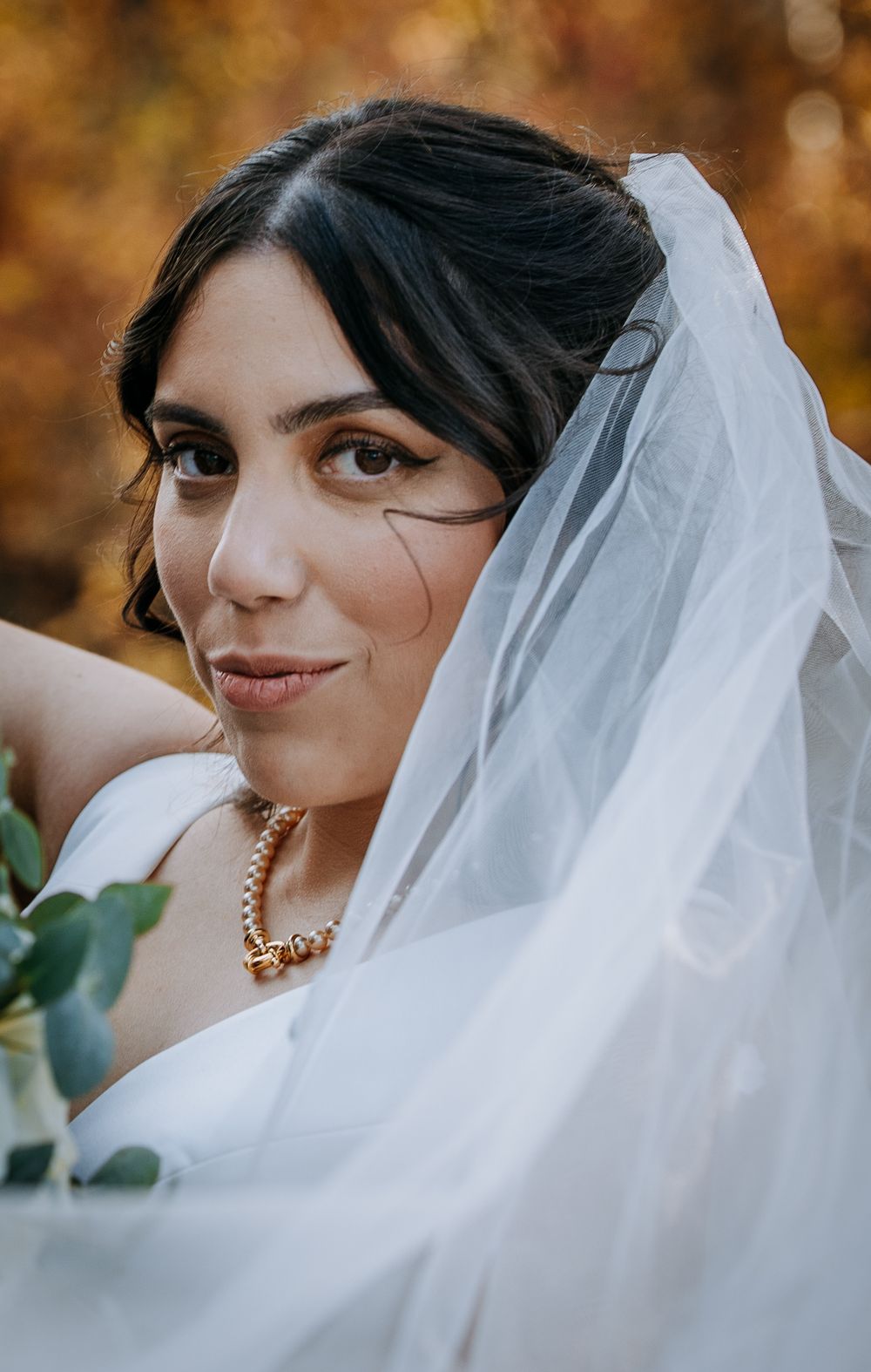 Elegant bridal portrait with flowing veil and pearl necklace against fall colors.