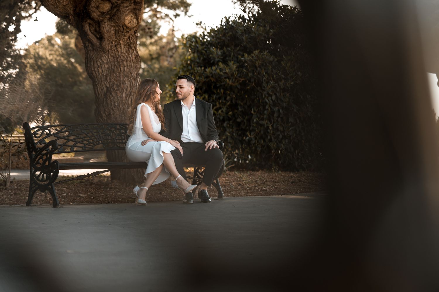 Artistic outdoor wedding photo taken through tree branches at golden hour.