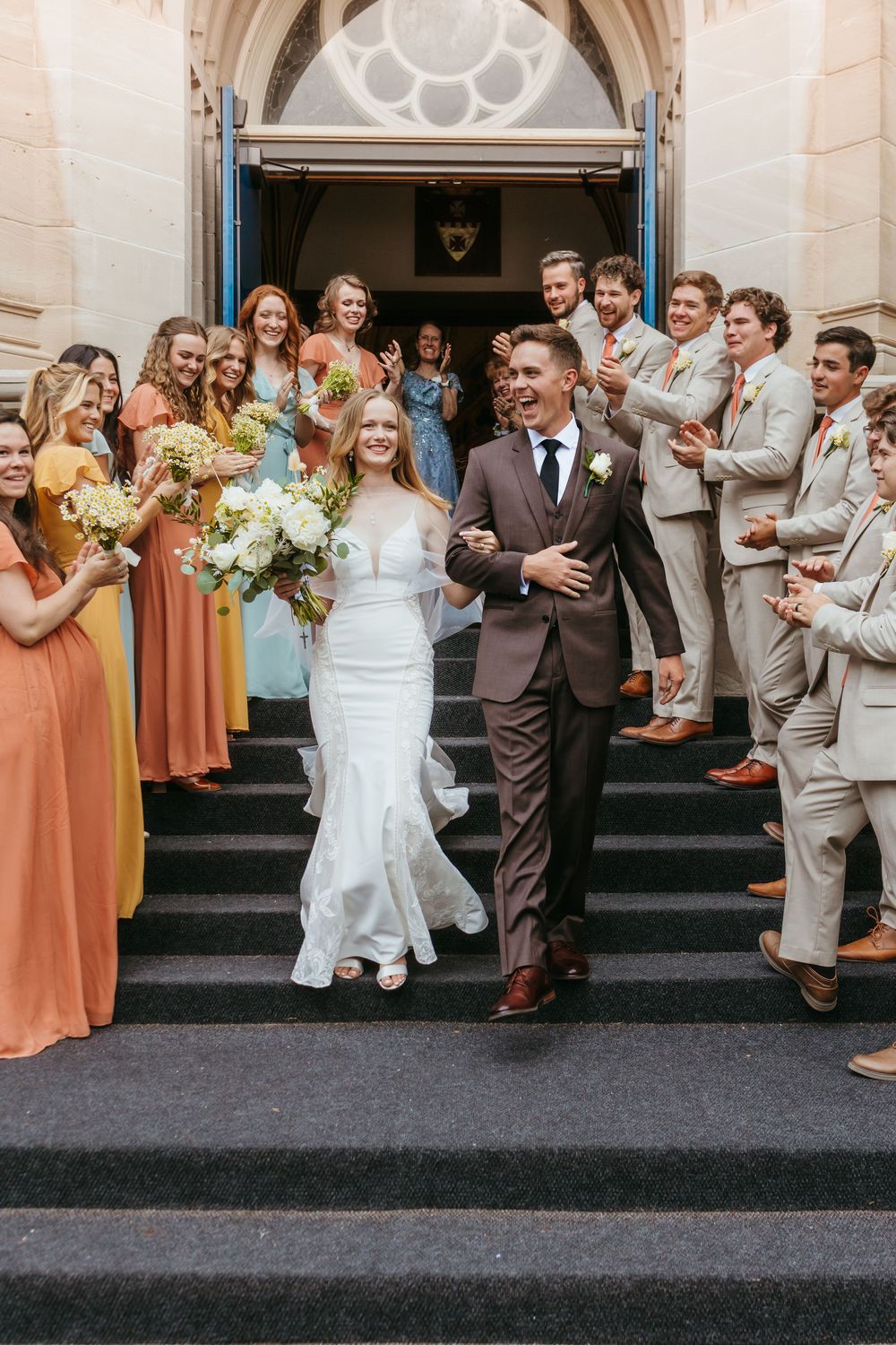 Wedding party celebration outside church with bridesmaids in peach dresses and groomsmen in suits.