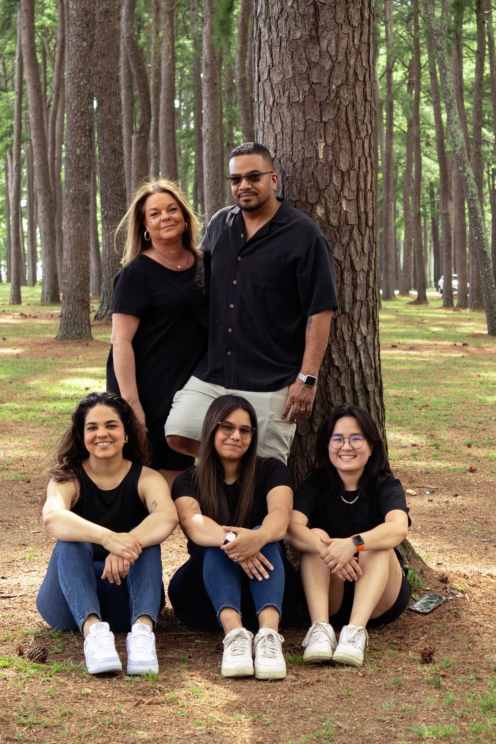 A Family sits together on fallen pine needles in a McFarland Park wearing matching black outfits.