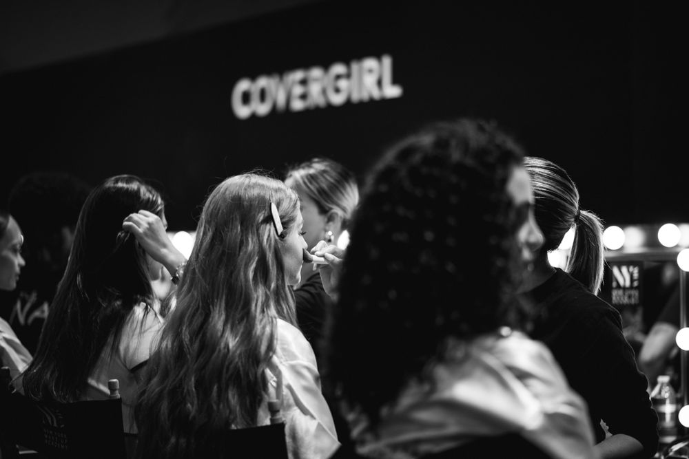 Black and white photo of a crowd at a Covergirl event or fashion show, with long-haired silhouettes in the foreground.