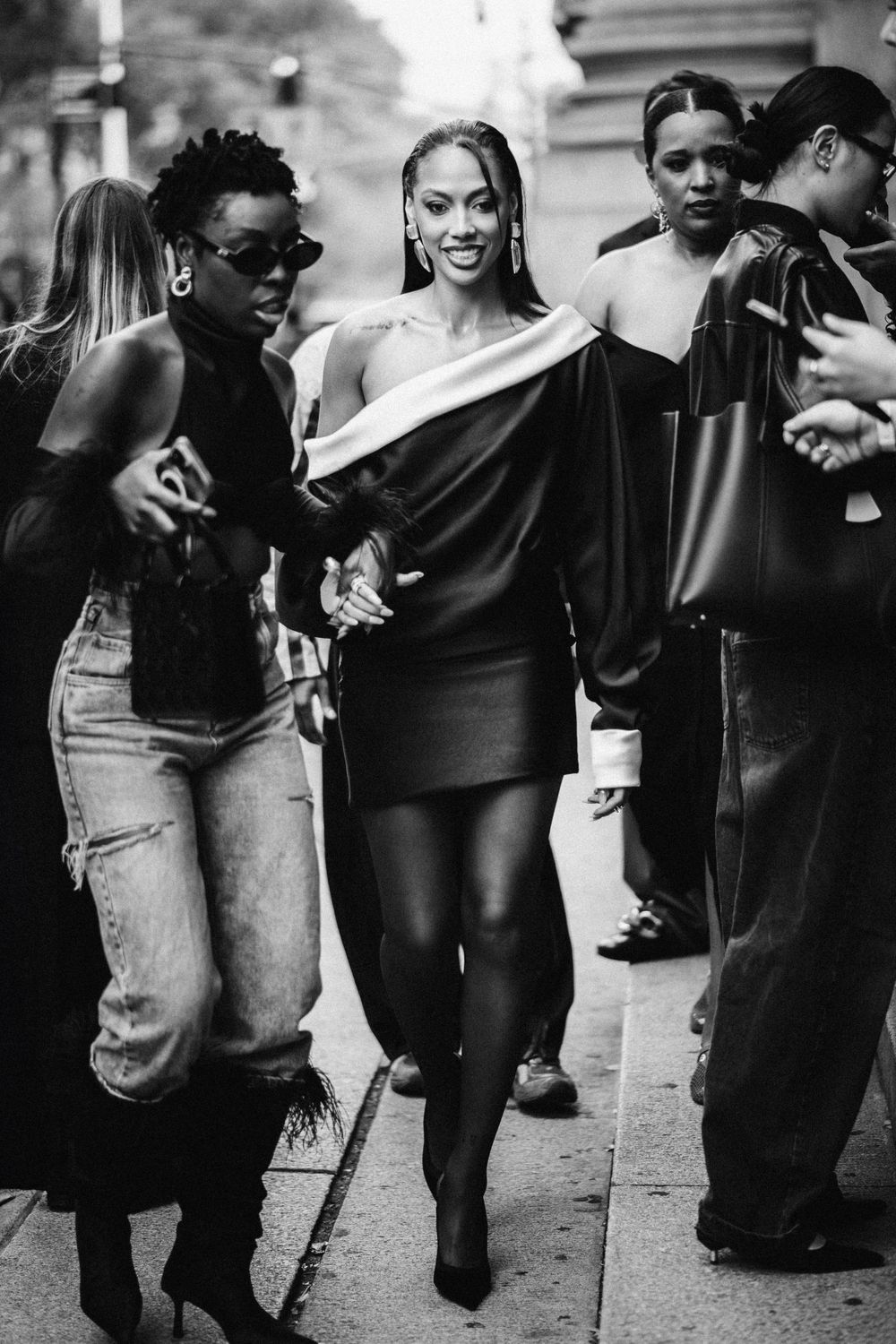 Black and white photo showing people walking and laughing together on a city street in casual and dressy attire.