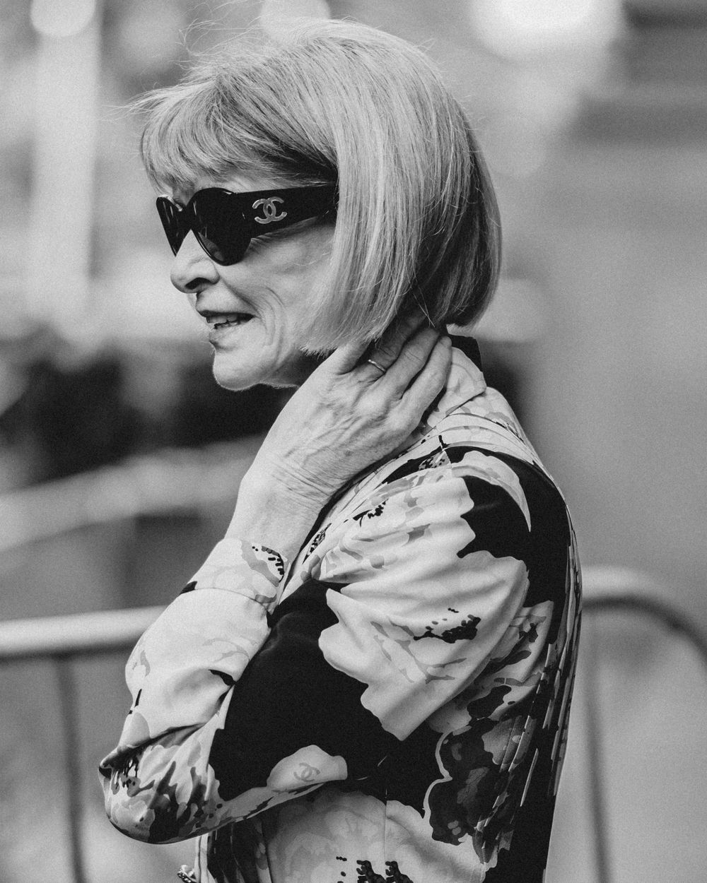 A black and white photo showing a stylish figure in designer sunglasses and a patterned outfit looking to the side.
