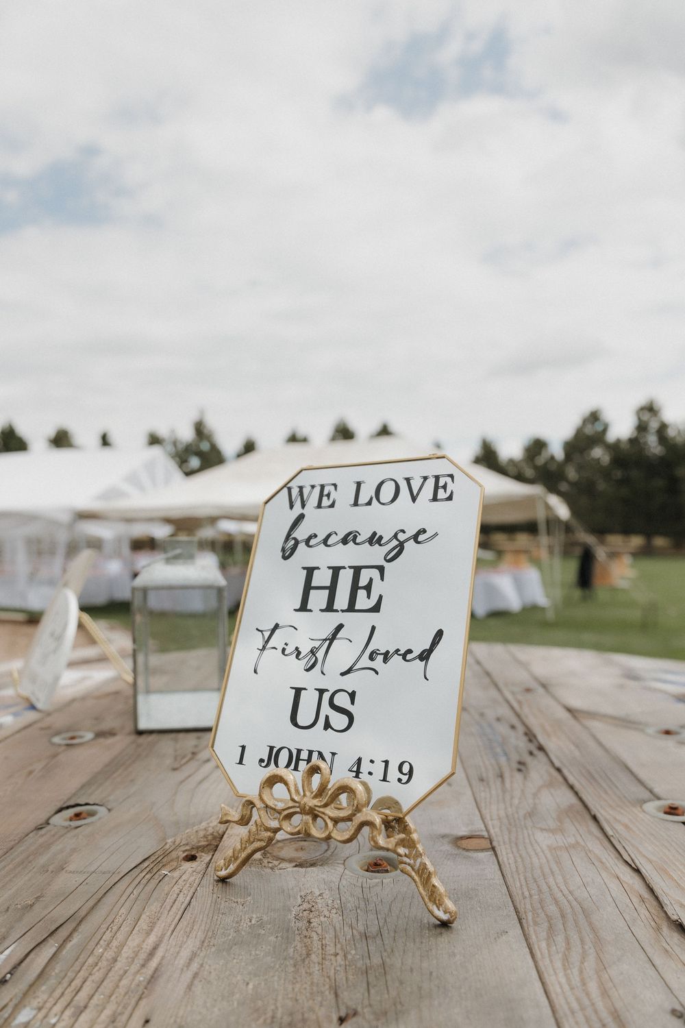 A series of white wooden signs with Bible verses and quotes arranged on rustic wooden planks at an outdoor wedding venue.