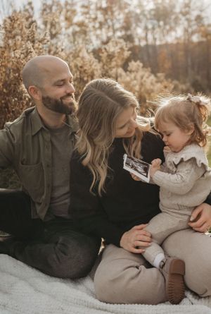 Family sits together on picnic blanket examining ultrasound photo during autumn sunset.