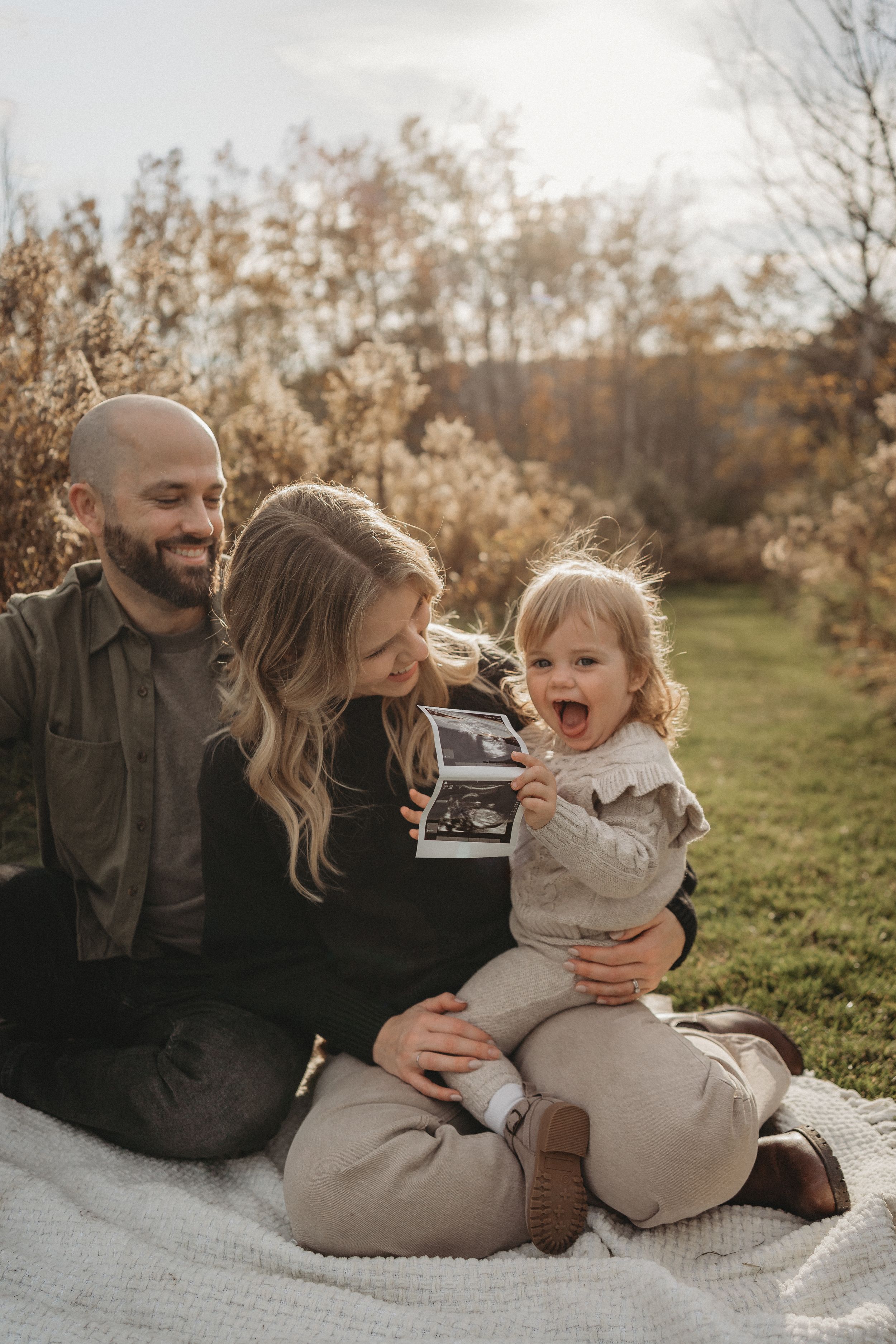 Happy family shares joyful laughter while looking at photos during outdoor autumn photoshoot.