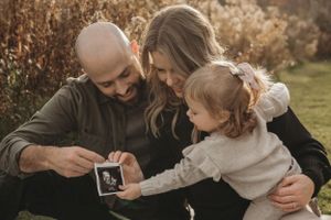 Family gathers closely on blanket outdoors to look at ultrasound photo together.
