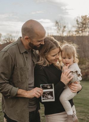 Family holding ultrasound photo during golden hour outdoor photoshoot.