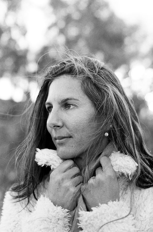 Black and white portrait of someone in a cozy white fleece looking contemplative against a blurred outdoor background.