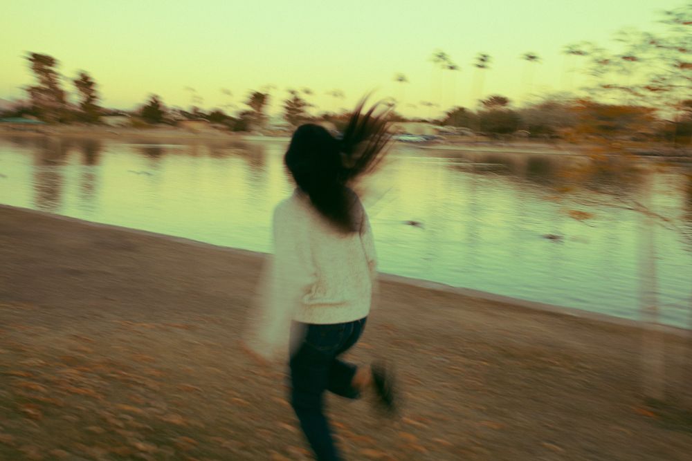 Cinematic running photo of girl chasing the wind at sunset, golden hour by the pond
