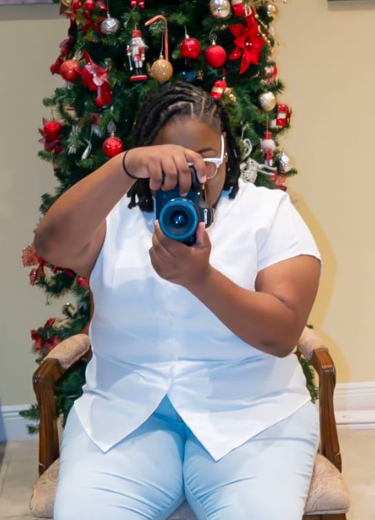 Professional photographer in white shirt taking photos by a decorated Christmas tree.