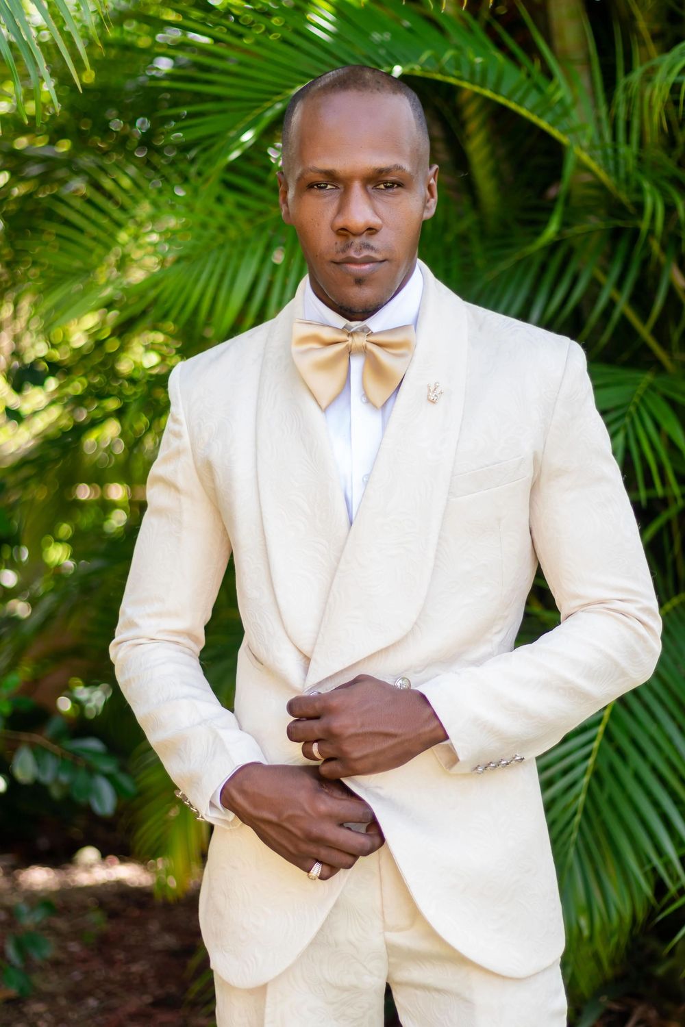 Elegant groomsmen wearing crisp white tuxedos pose against a lush tropical palm background.