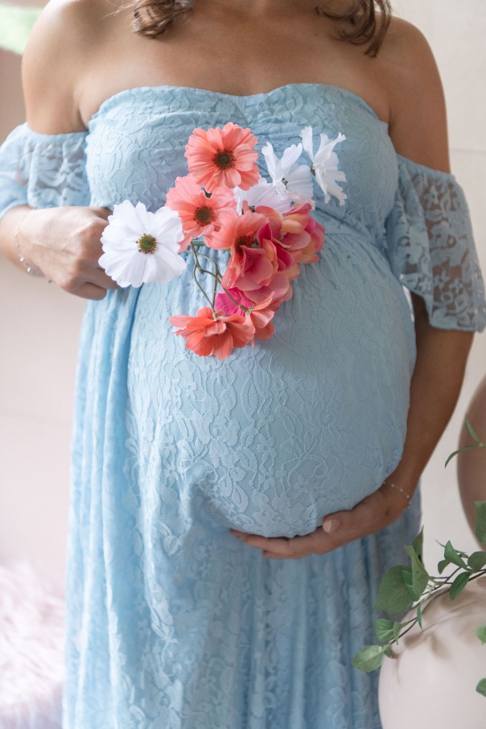 A light blue lace maternity dress adorned with coral and white flowers highlights a pregnancy bump.