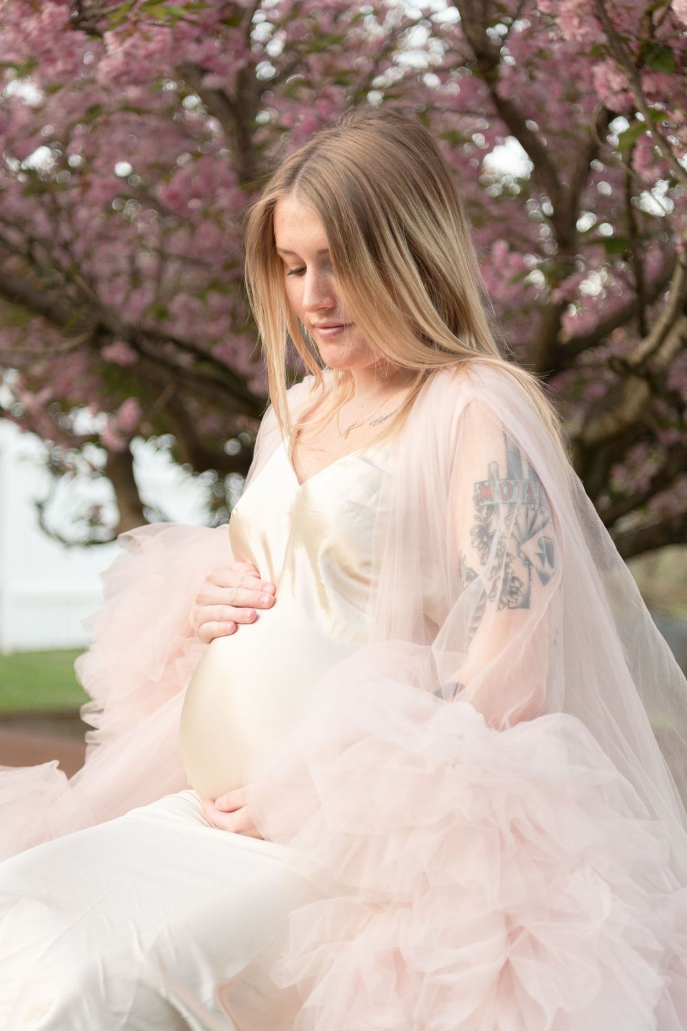 An ethereal maternity portrait with pink cherry blossoms in the background.