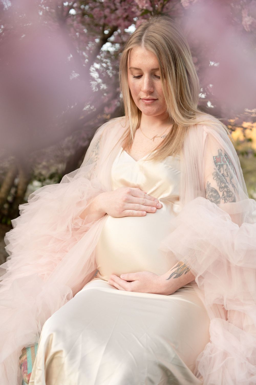 A serene maternity moment captured beneath blooming spring cherry blossoms.