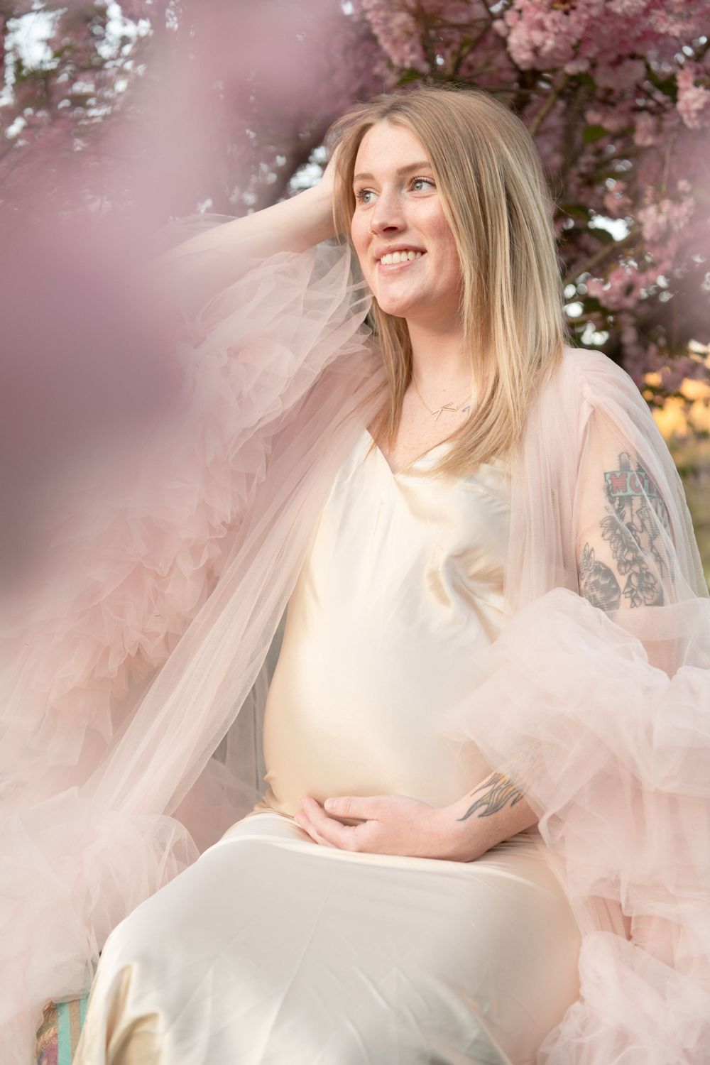 A joyful maternity portrait surrounded by pink cherry blossoms in spring.