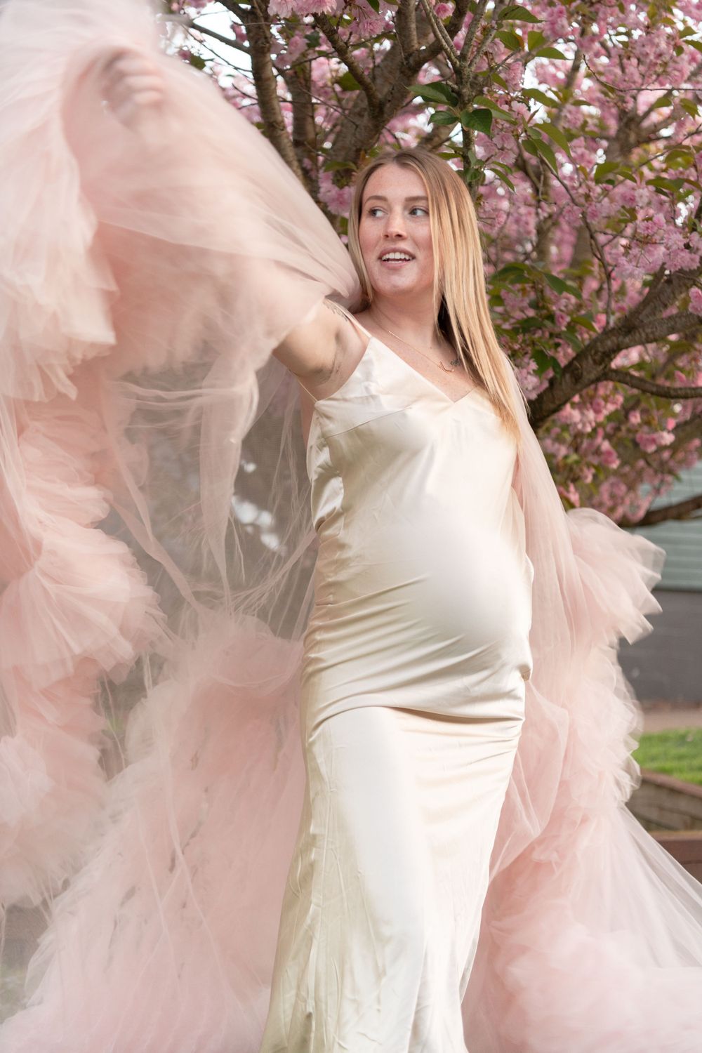 A dramatic maternity portrait with flowing pink tulle against flowering trees.