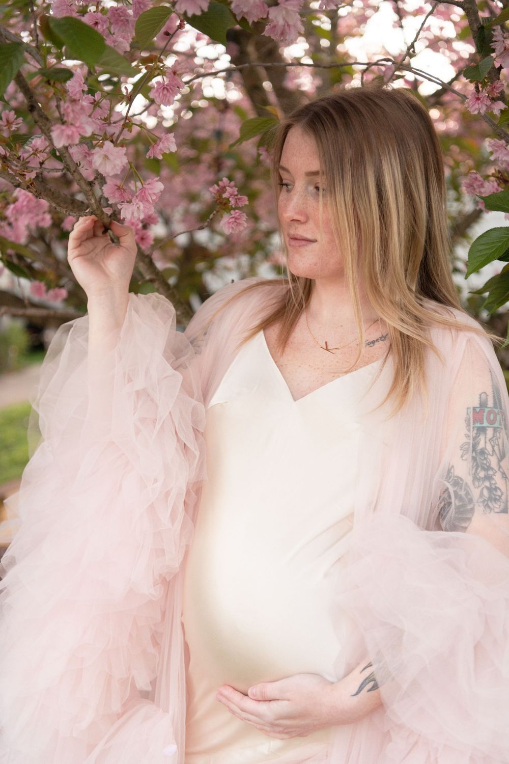 A peaceful maternity portrait among pink cherry blossoms in full bloom.