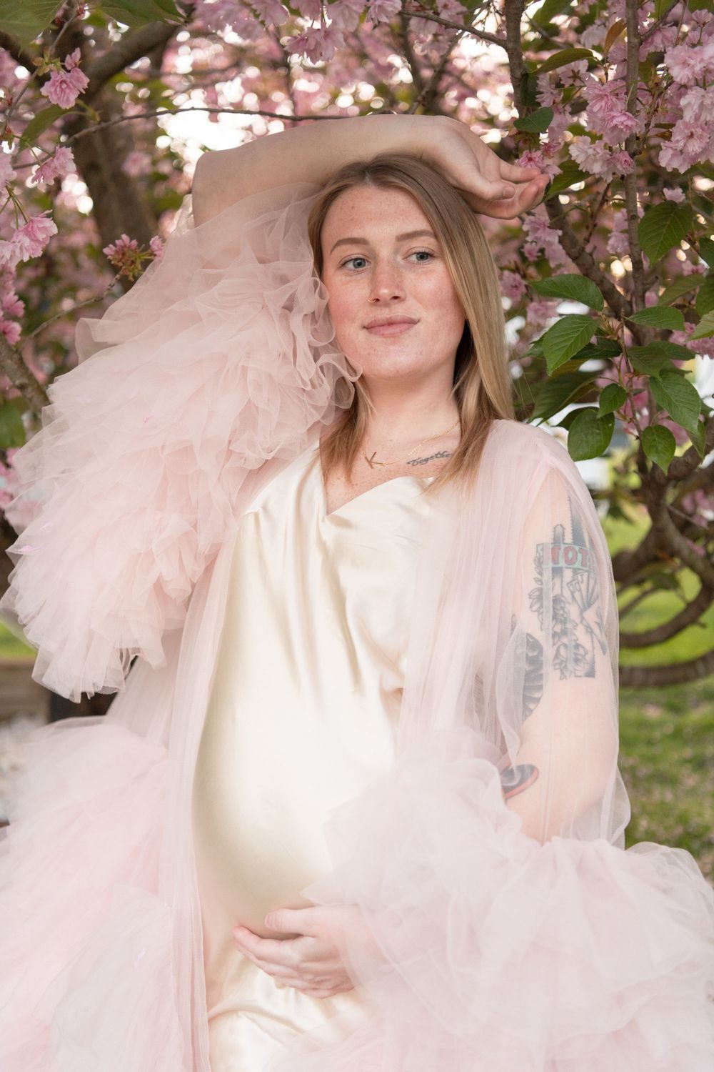 A radiant maternity portrait framed by delicate pink cherry blossoms.