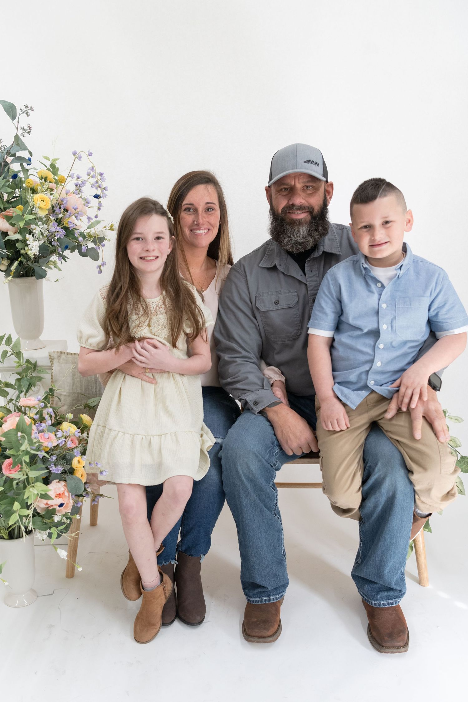 Family of four sitting together on bench surrounded by floral arrangements.