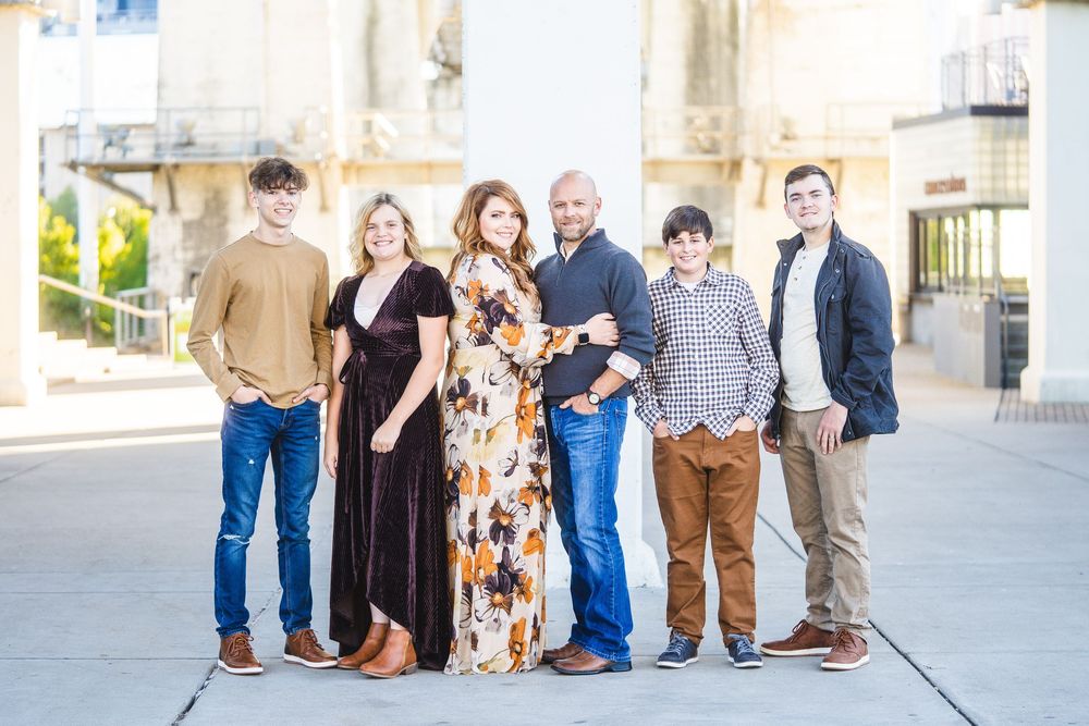Extended family in casual clothing poses together on stone steps outside a building during a gathering.