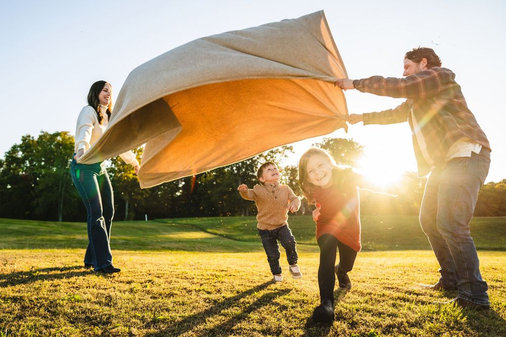 Family plays with a white blanket in a sunny field during golden hour.