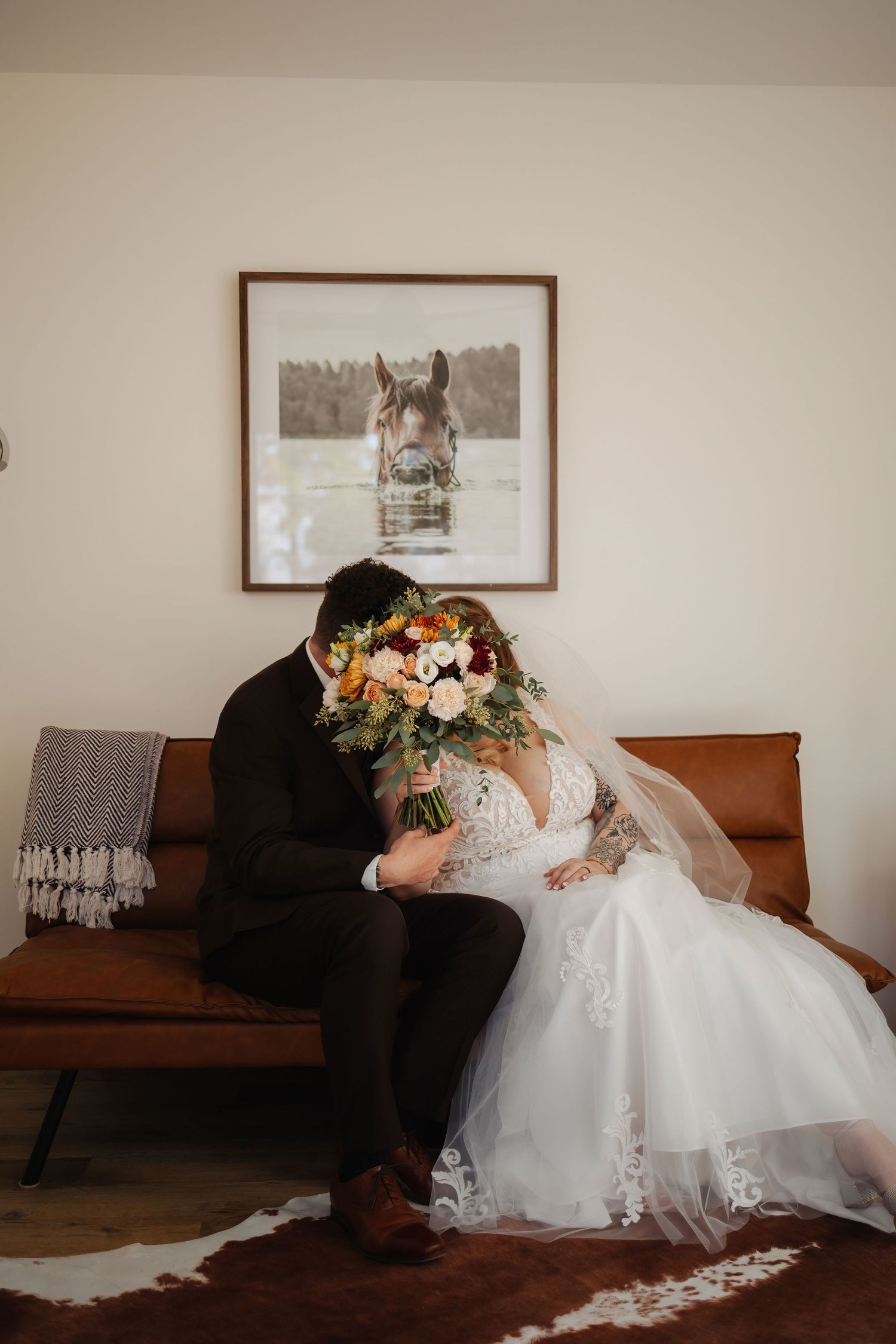 Couple resting on brown leather couch in intimate indoor setting.