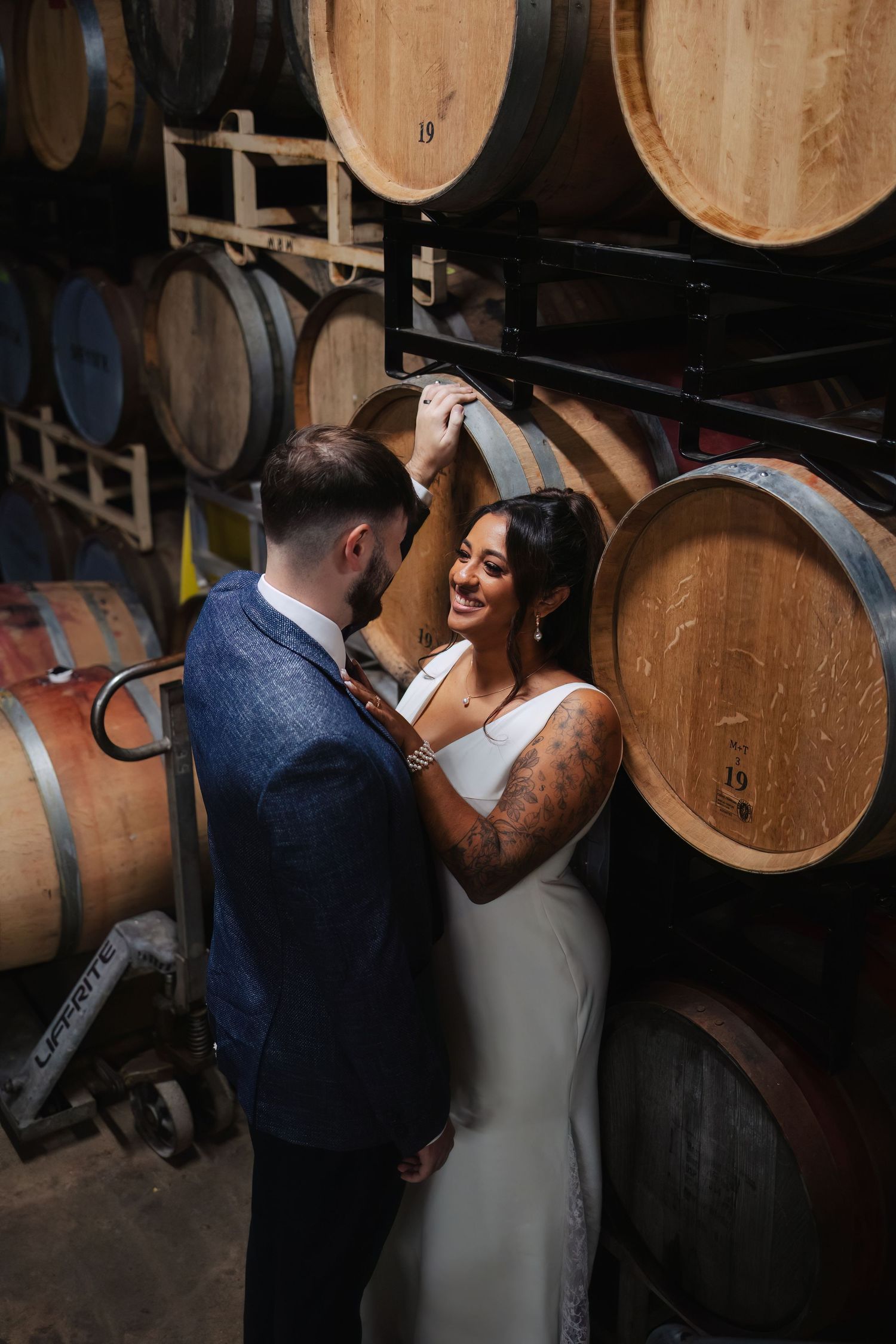 A romantic moment between newlyweds in a rustic wine cellar with wooden barrels.