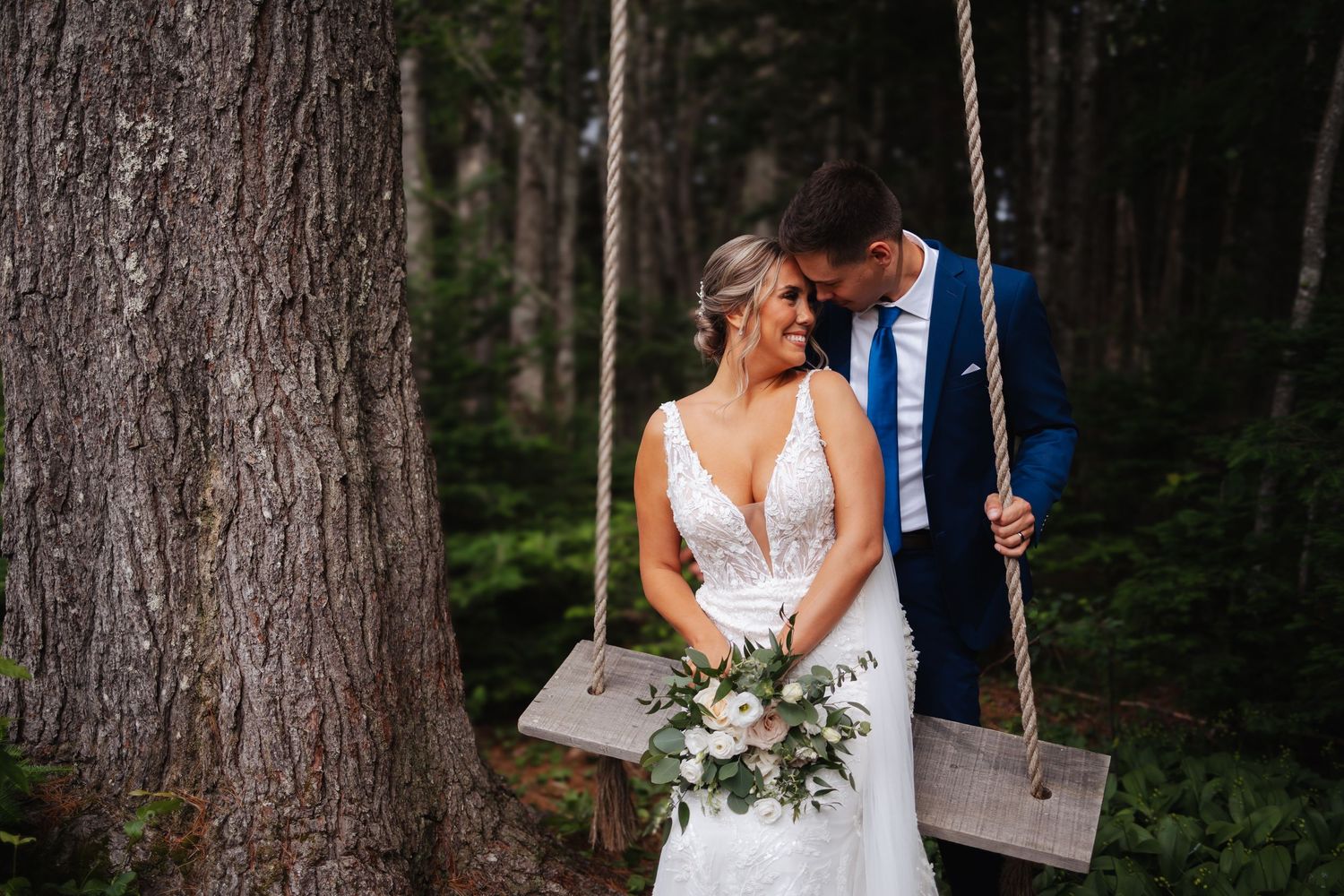 Newlyweds sharing an intimate moment on a rustic wooden swing in a forest setting.