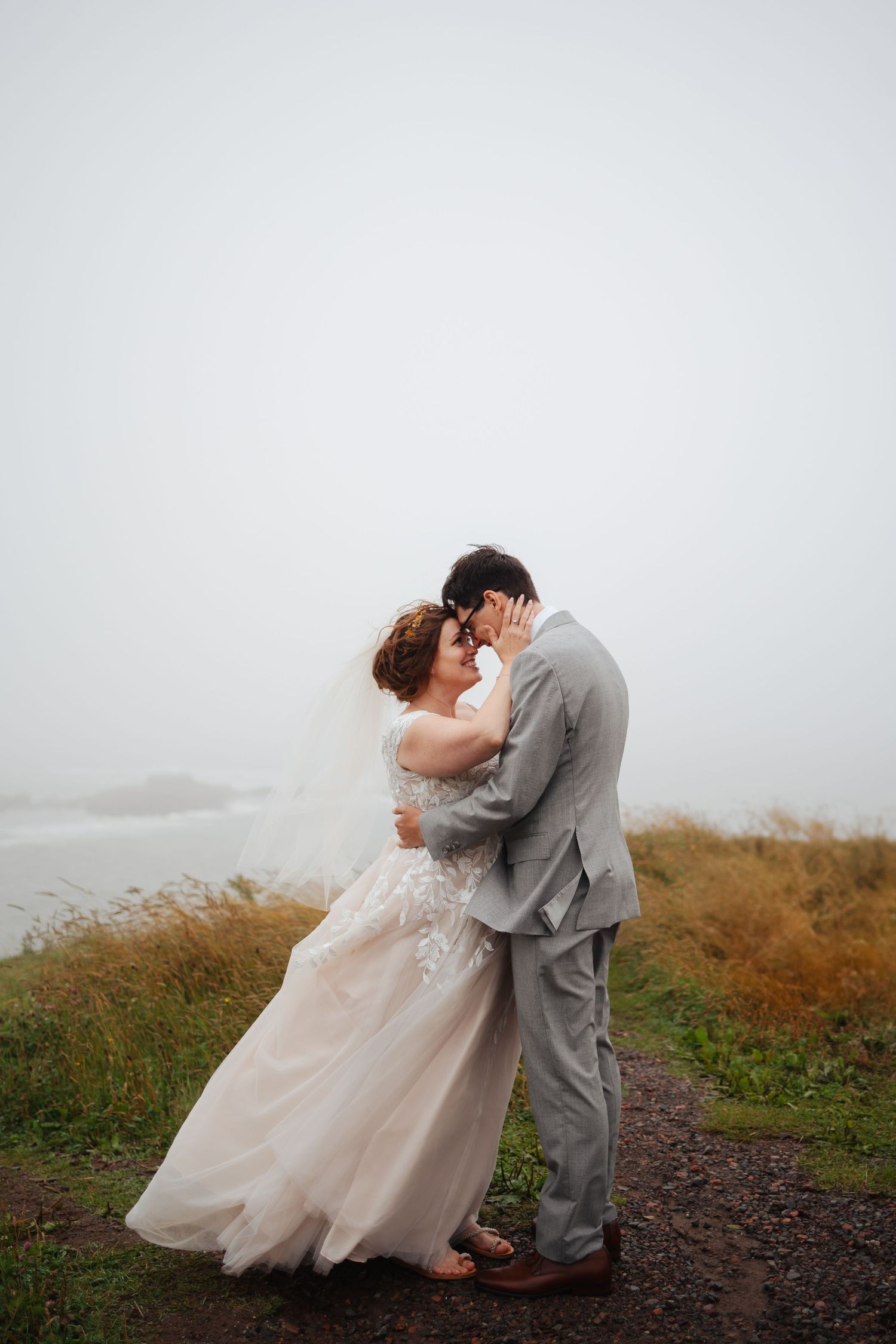 A couple shares an intimate dance in their wedding attire on a misty hillside.