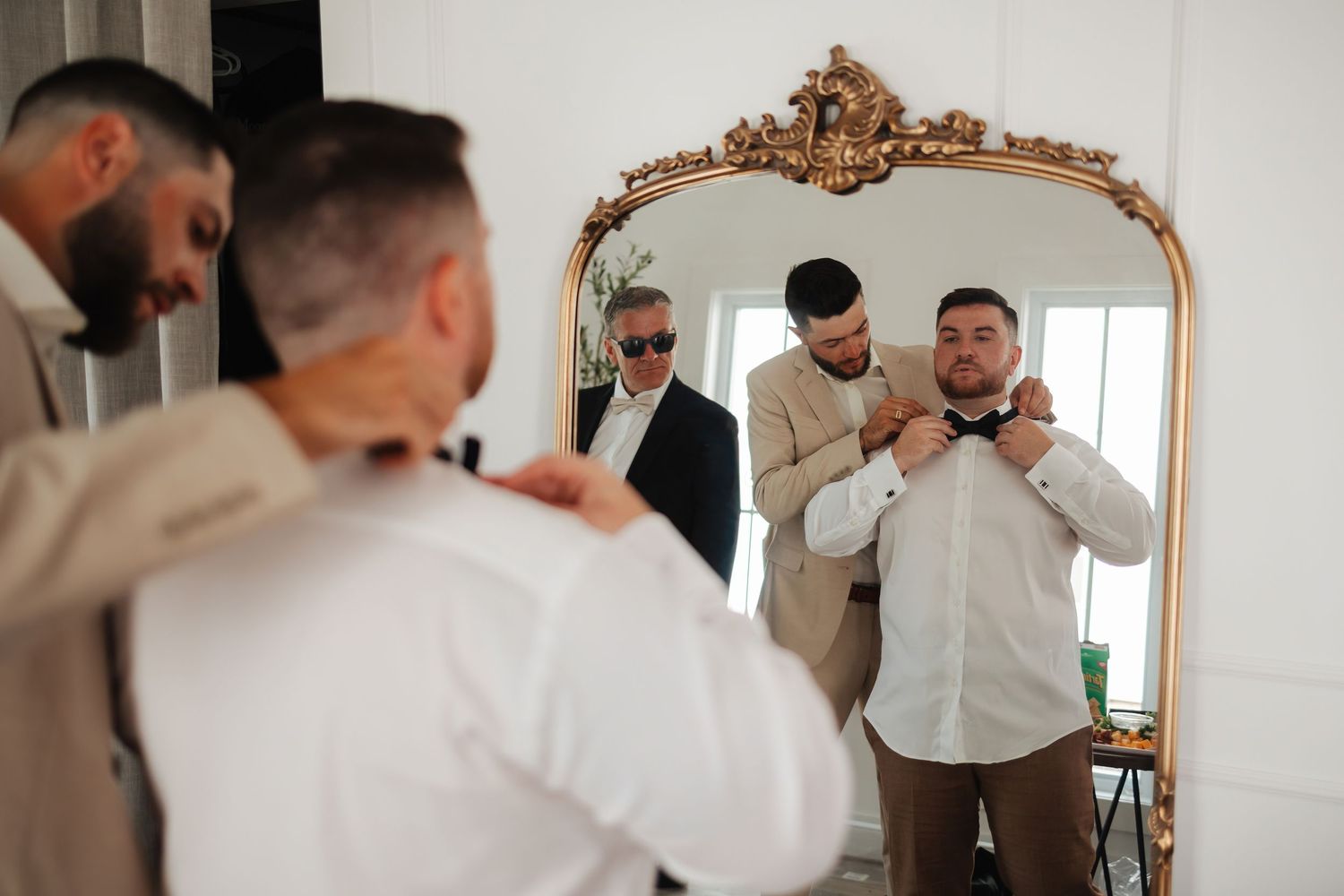 Getting ready scene with formal attire and ornate gold mirror in bright white room.