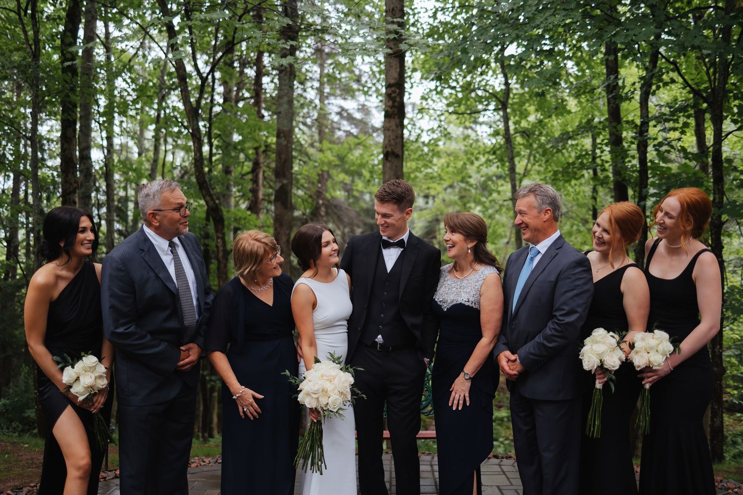 Wedding party gathers for a group photo in a wooded setting.