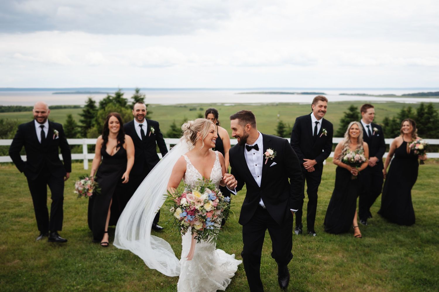 Wedding party members in formal attire pose against a scenic coastal backdrop.