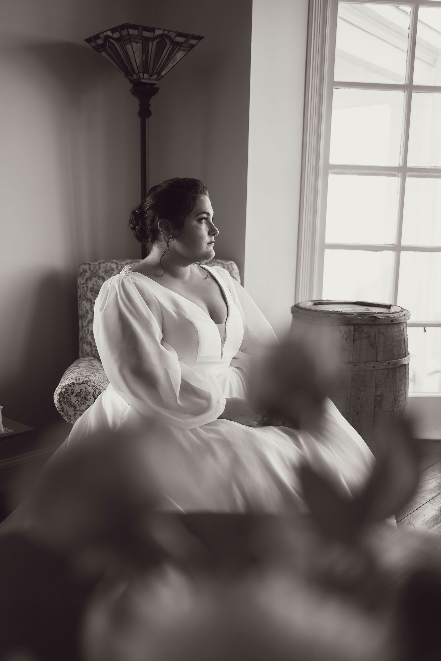 Artistic black and white bridal portrait by a window with dramatic lighting.