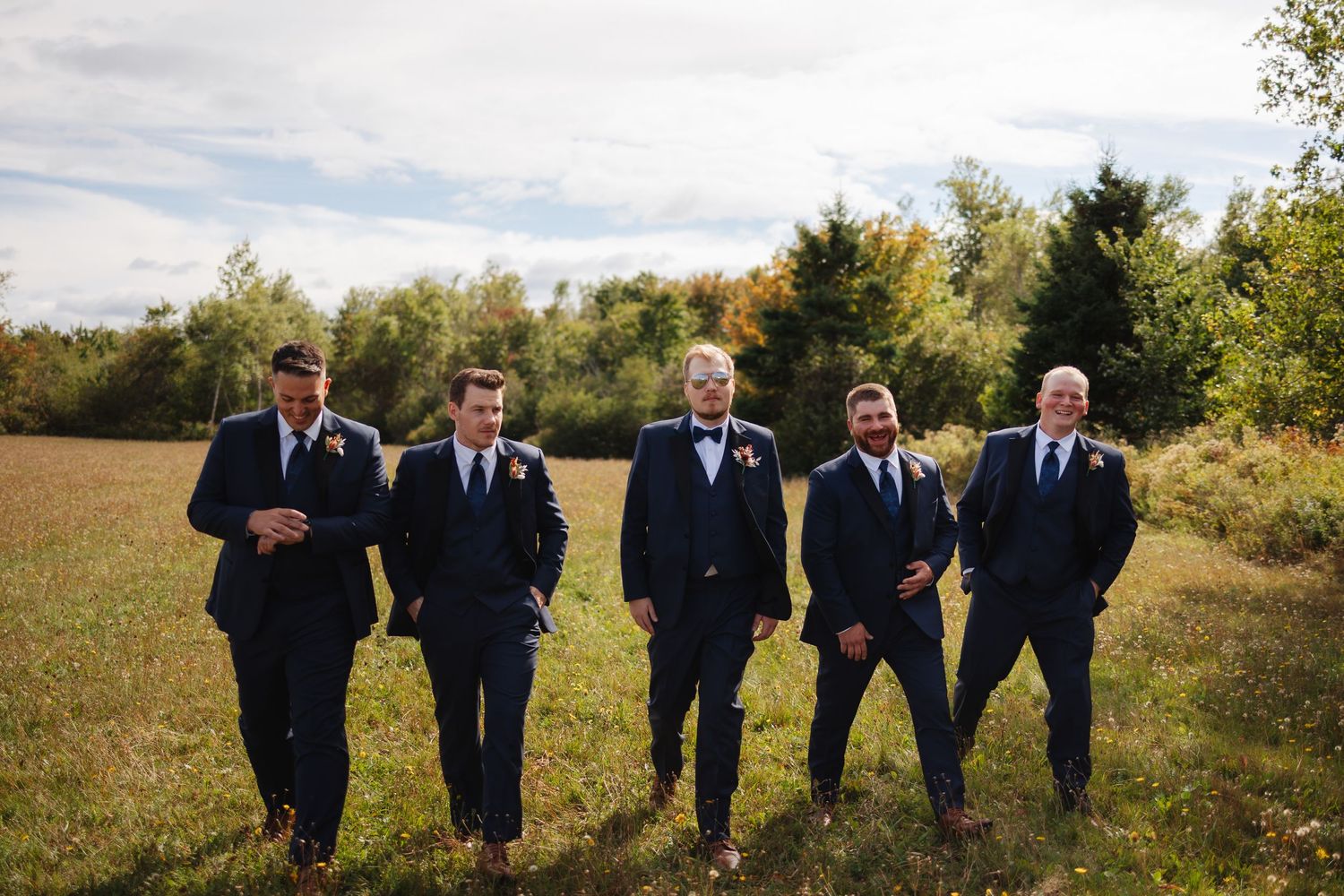 Groomsmen in navy suits pose confidently in an autumn field with trees in the background.