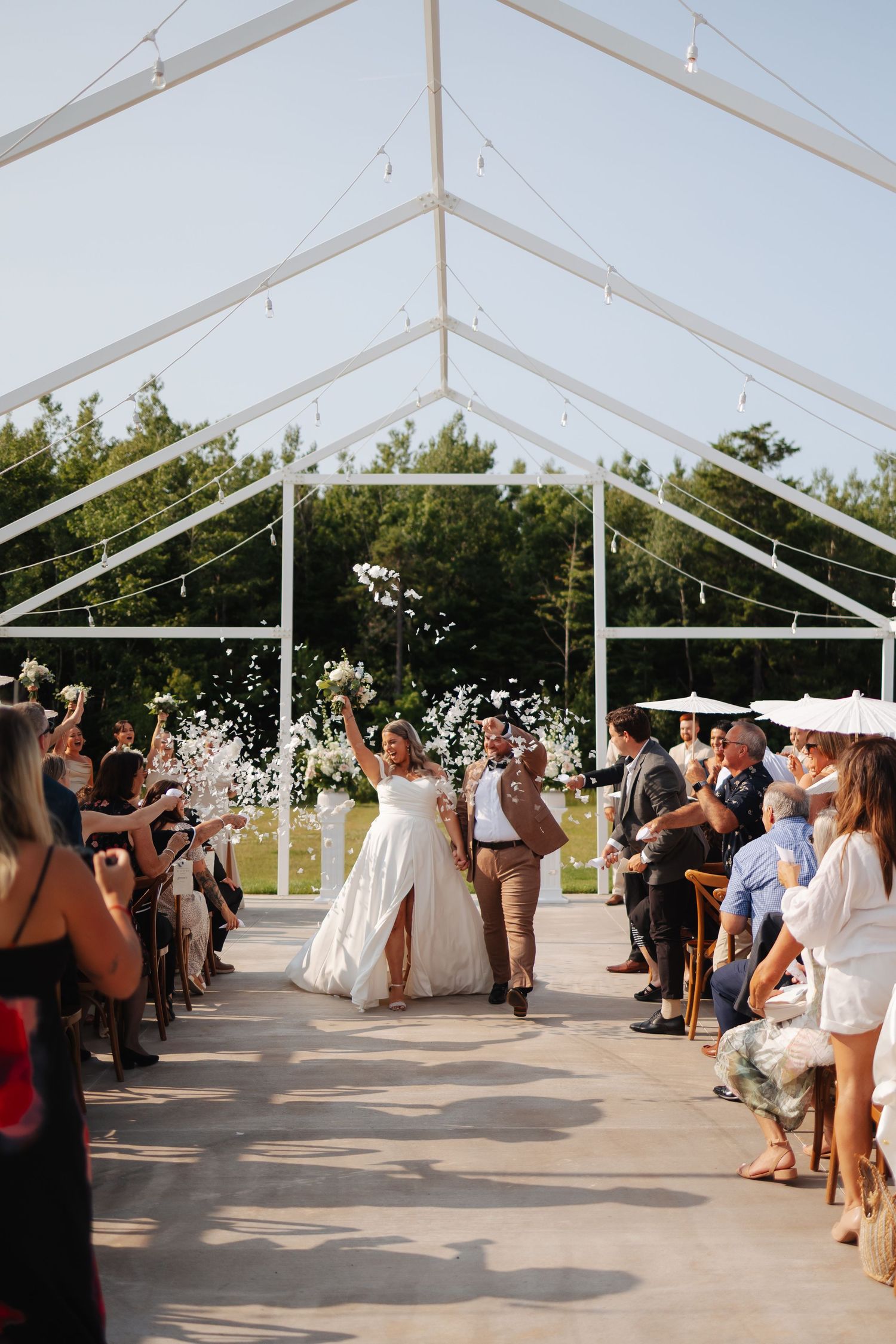 Clear tent wedding venue with guests throwing confetti during celebration.