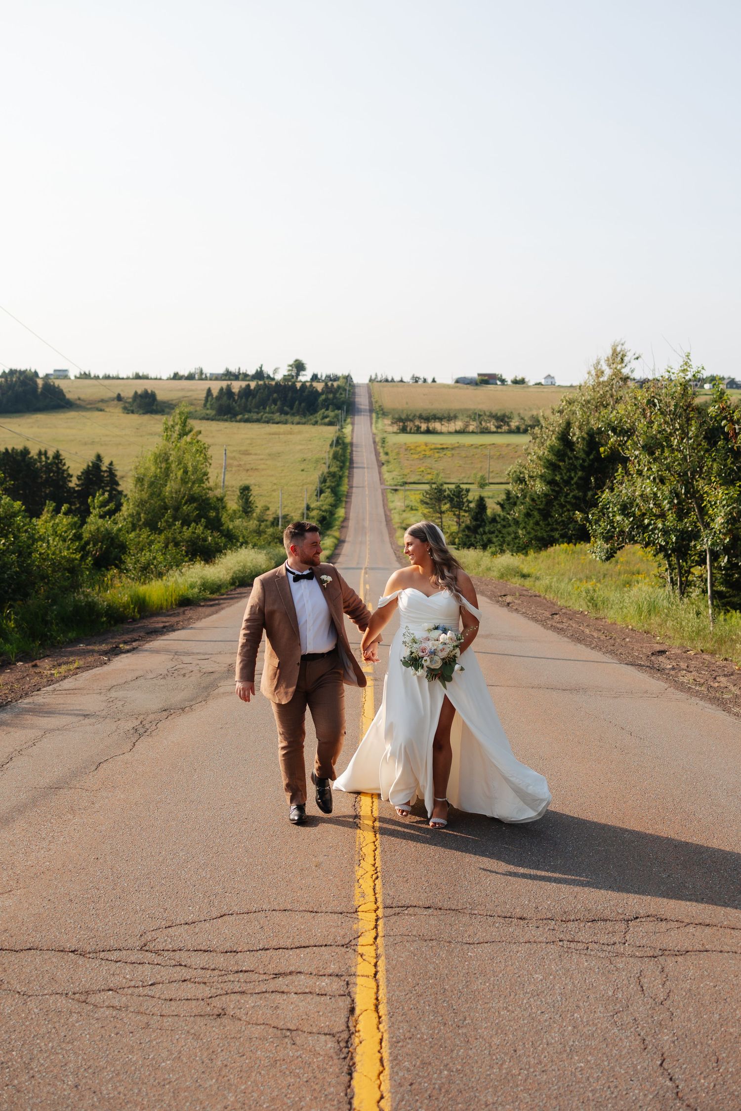 Couple posing on rural road with fields and blue sky in background.