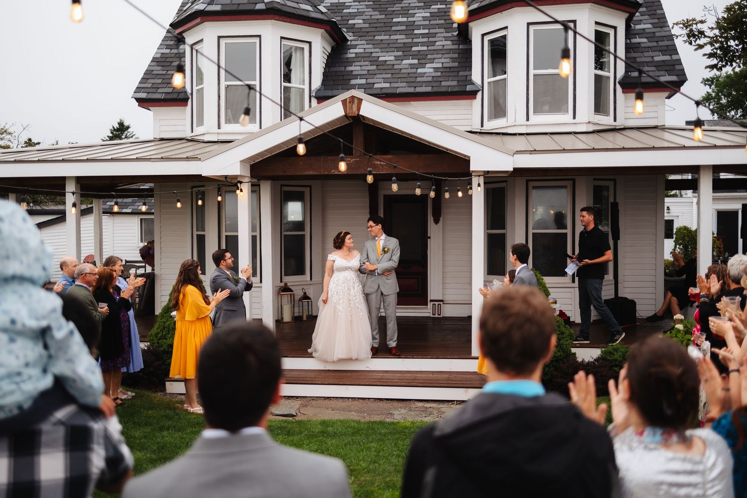A charming white house with string lights hosts an outdoor wedding celebration.