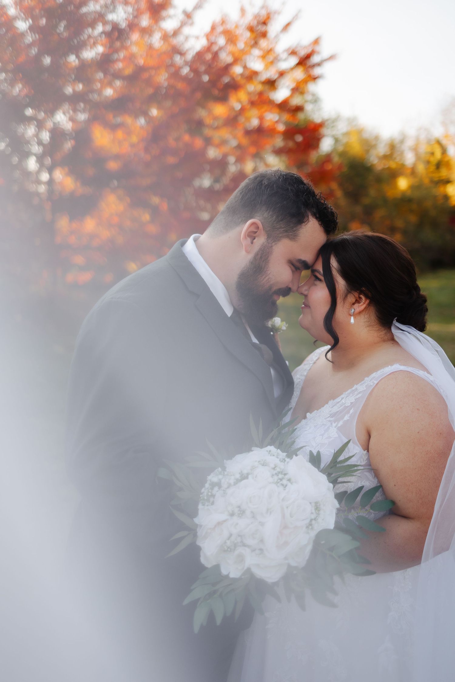 Romantic autumn wedding portraits with soft focus and fall foliage in the background.