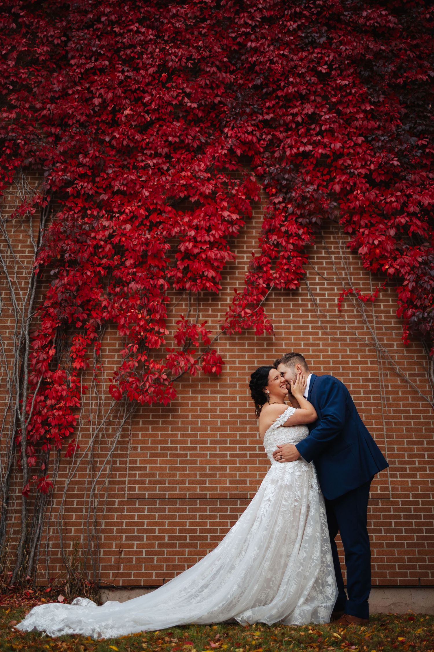 A romantic wedding portrait against a brick wall with vibrant red autumn foliage.
