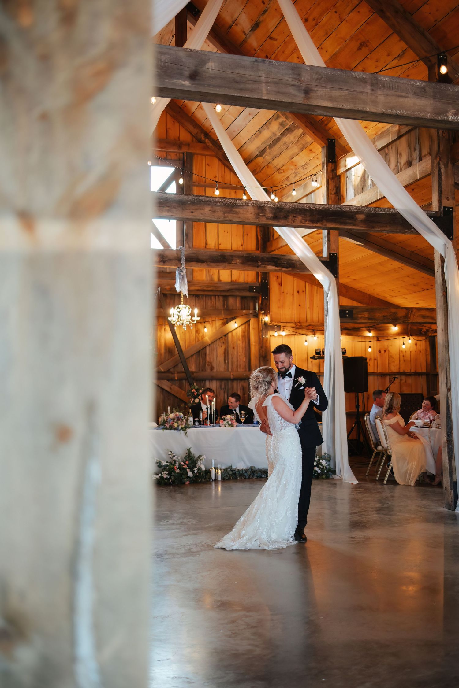 A couple shares their first dance in a rustic wooden barn venue with exposed beams.