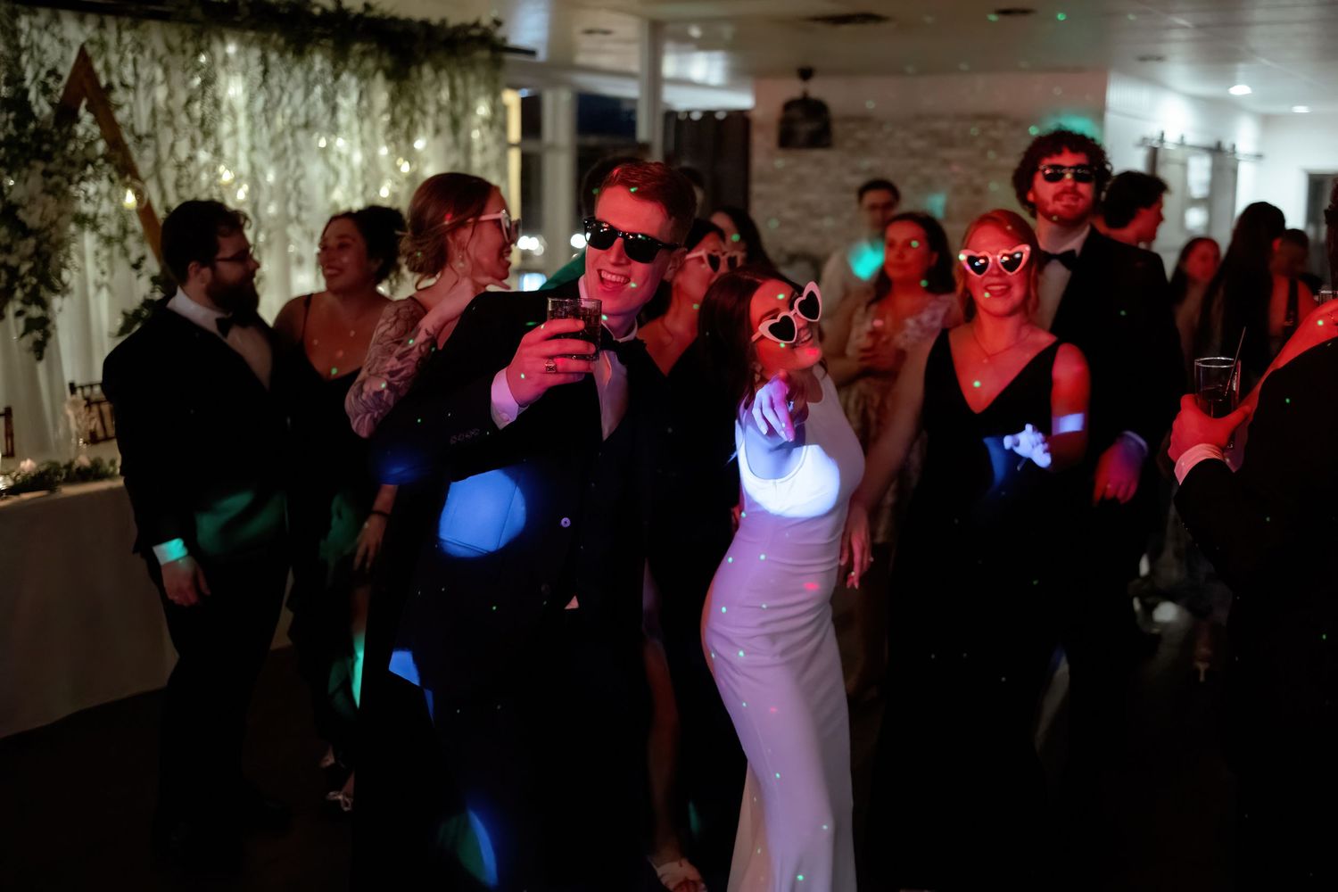 Dance floor filled with silhouettes of wedding guests under colorful party lighting.